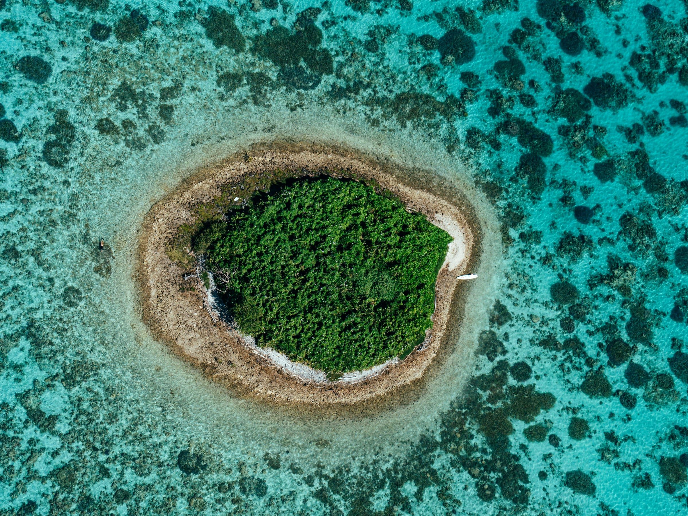 Un îlot boisé vu à la verticale, ceinturé de sable et de corail dans le lagon calédonien.