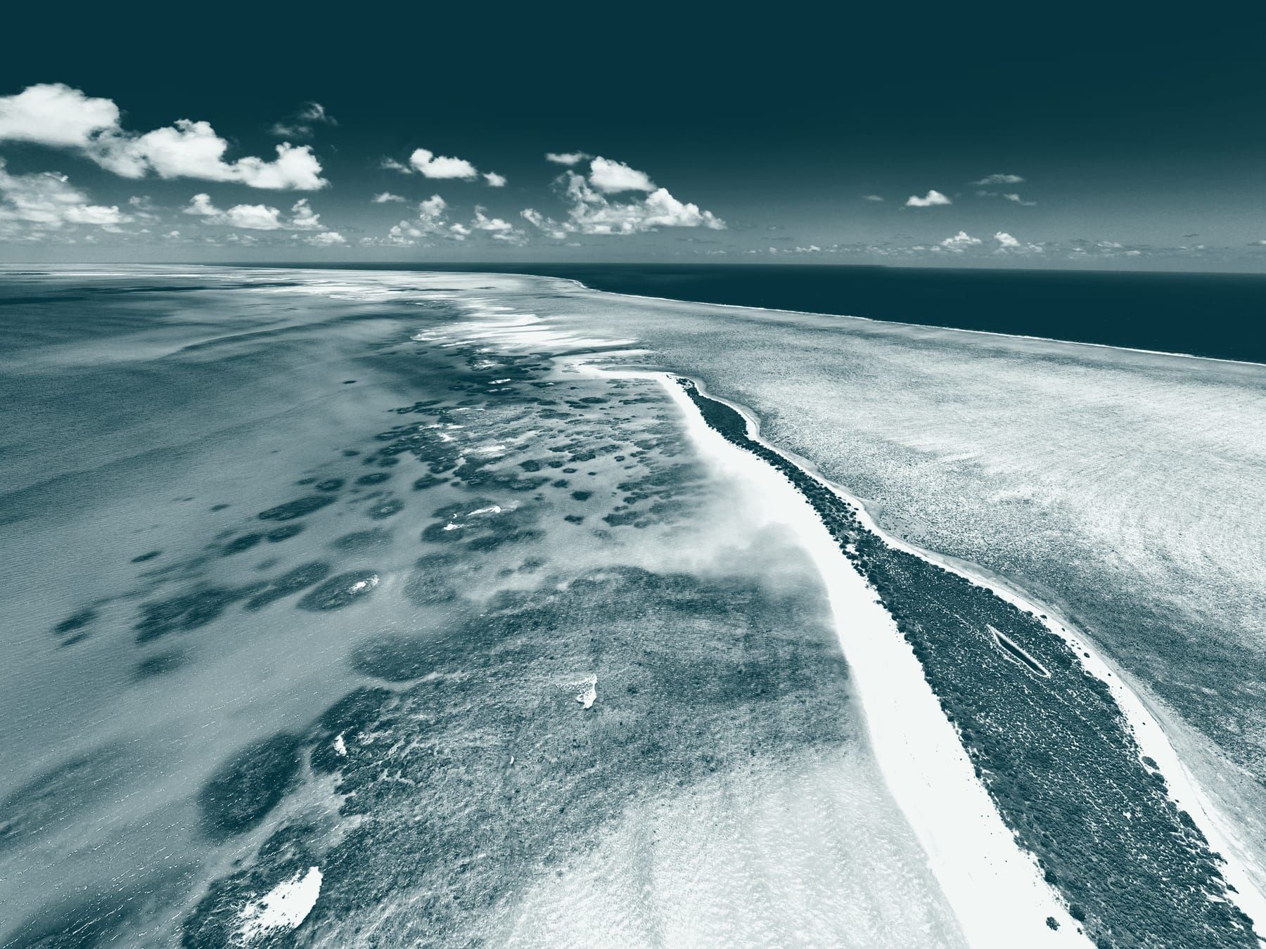 Une longue langue de sable sépare le platier corallien de l’océan profond.