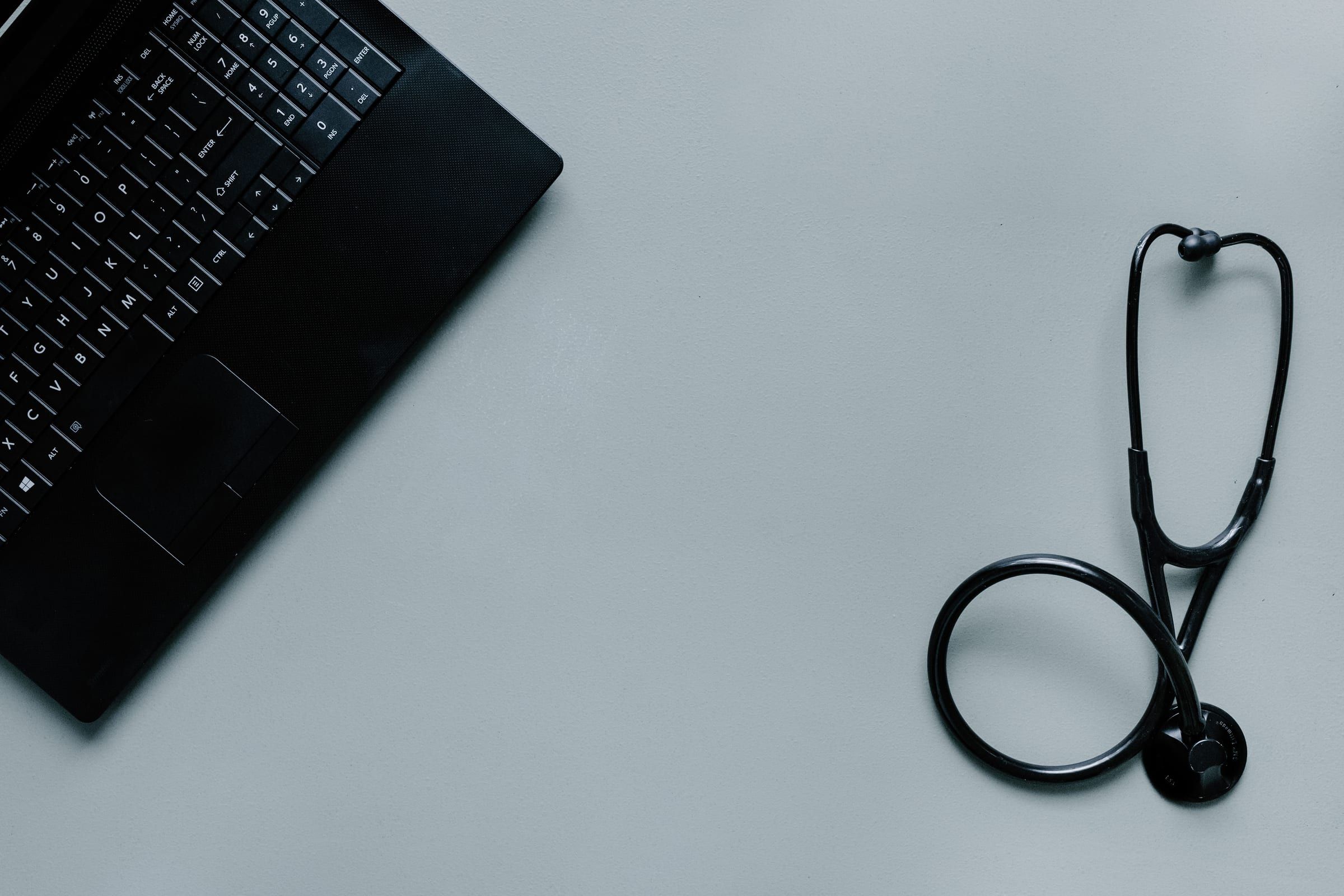 Un ordinateur portable et un stéthoscope posés sur un plan de travail.