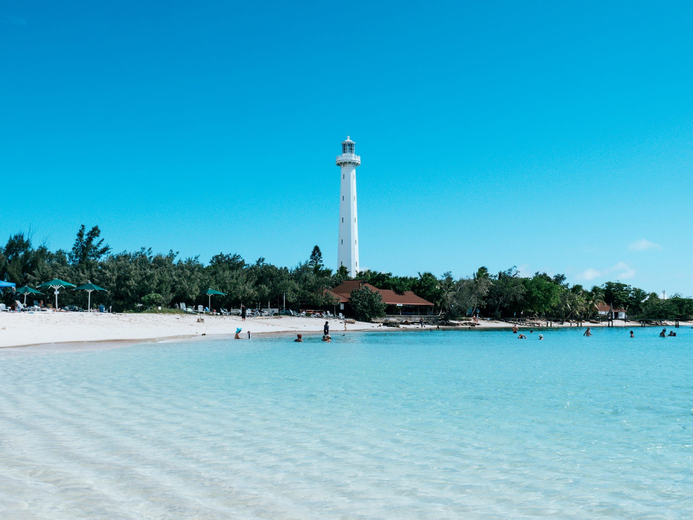 Un phare blanc domine une plage bordée de filaos et une eau très claire.