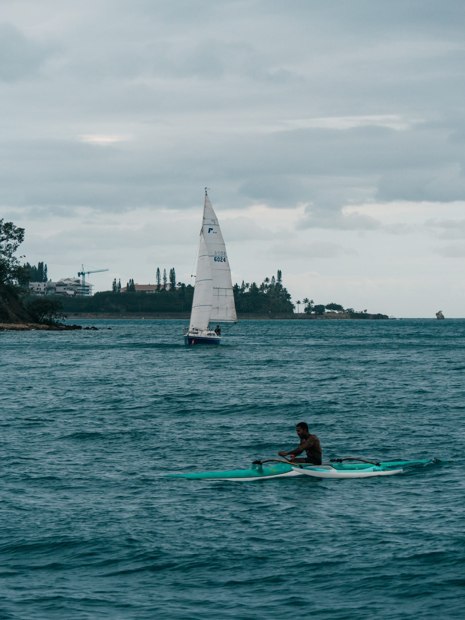 Un rameur en pirogue à balancier croise un voilier dans la rade de Nouméa.
