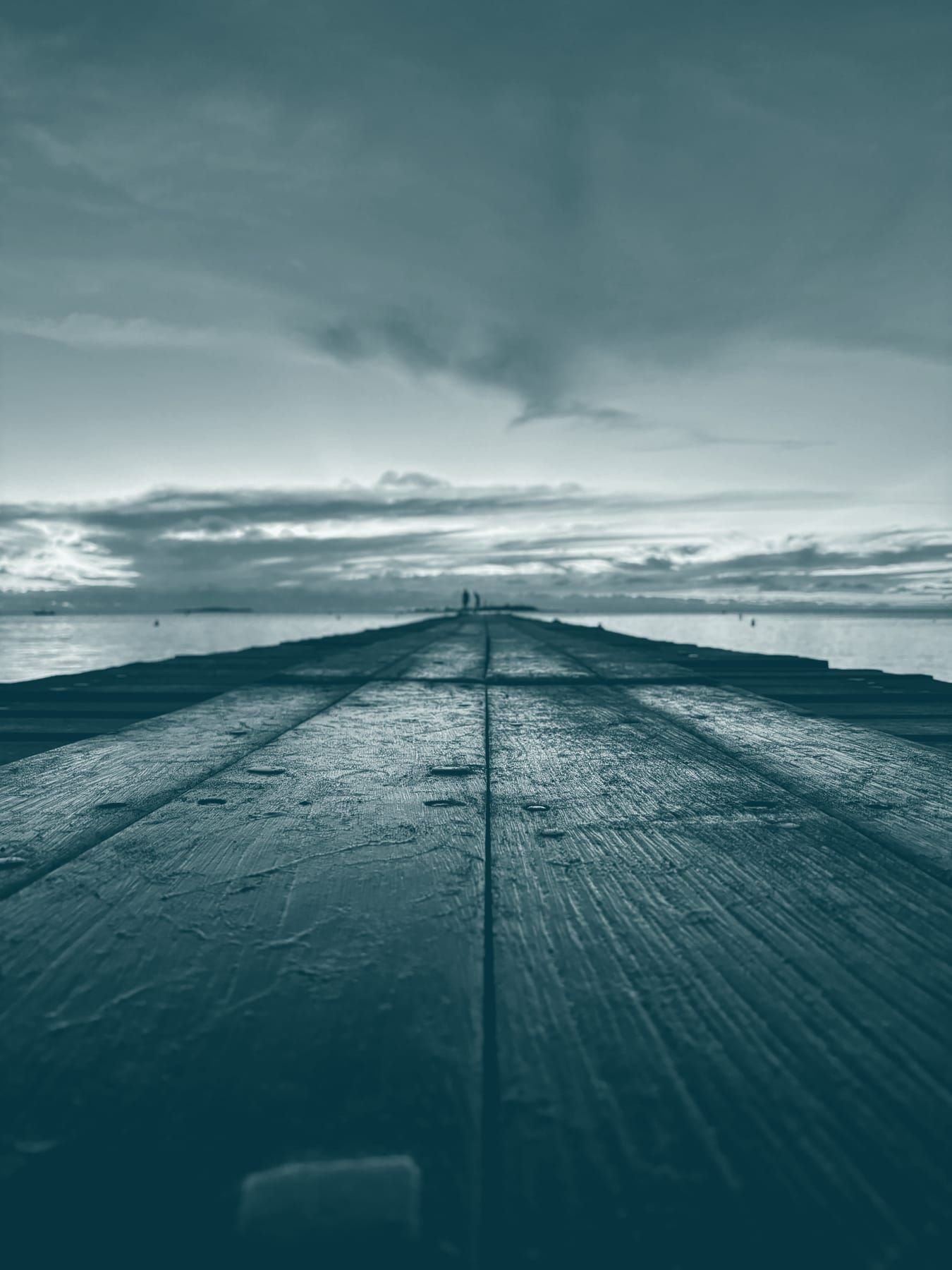 Un ponton de bois file vers l’horizon au coucher du soleil, deux silhouettes au bout.